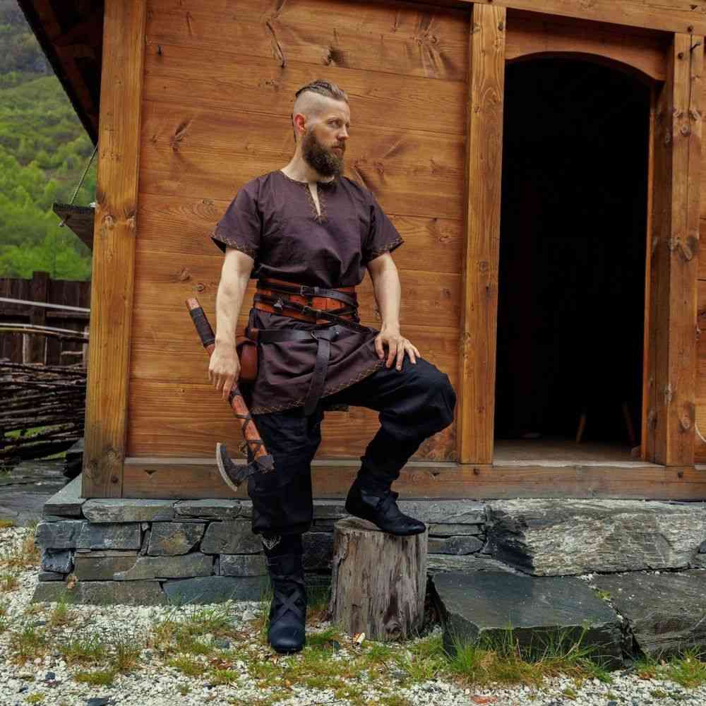 Man in black linen Pirate pants with tapered, lace-up legs, brown tunic, and leather belt, holding an axe.