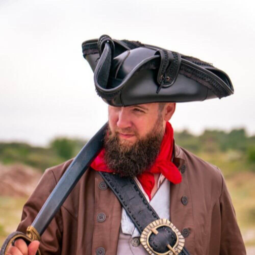 Bearded man in a red scarf wearing a classic ornate pirate hat and brown coat, holding a curved sword over his shoulder.