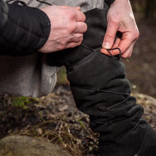 Hands lacing up black suede Pirate gaiters, transforming shoes into knee-high pirate boots.
