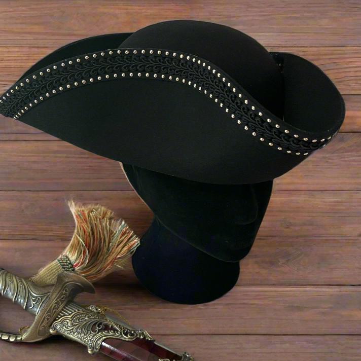 Handmade black Pirate tricorn hat with gold stud and scroll trim, displayed on a stand.