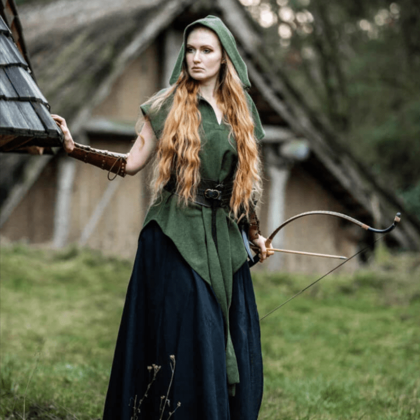Pirate woman in a green hooded cotton tunic with a belt, holding a bow, standing in a rustic setting.