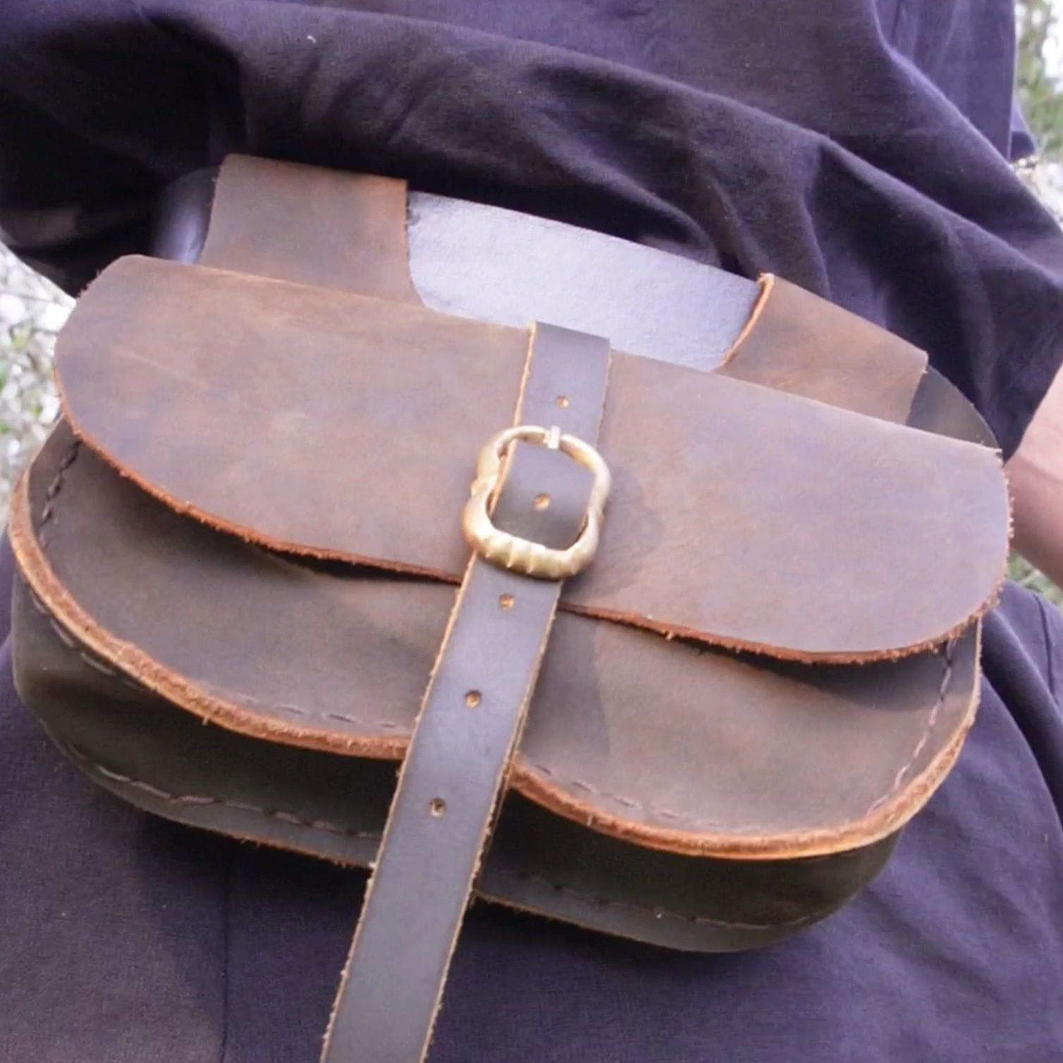 Brown full-grain leather Pirate belt pouch with an antique brass buckle closure, worn on a black garment.