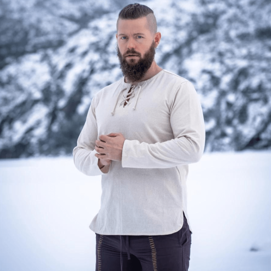 Man in a natural cotton long-sleeve Pirate tunic with a lace-up collar, standing in snow.