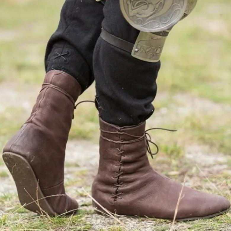 Brown low-cut pirate boots with lace-tied faux leather, worn over black pants on grassy ground.