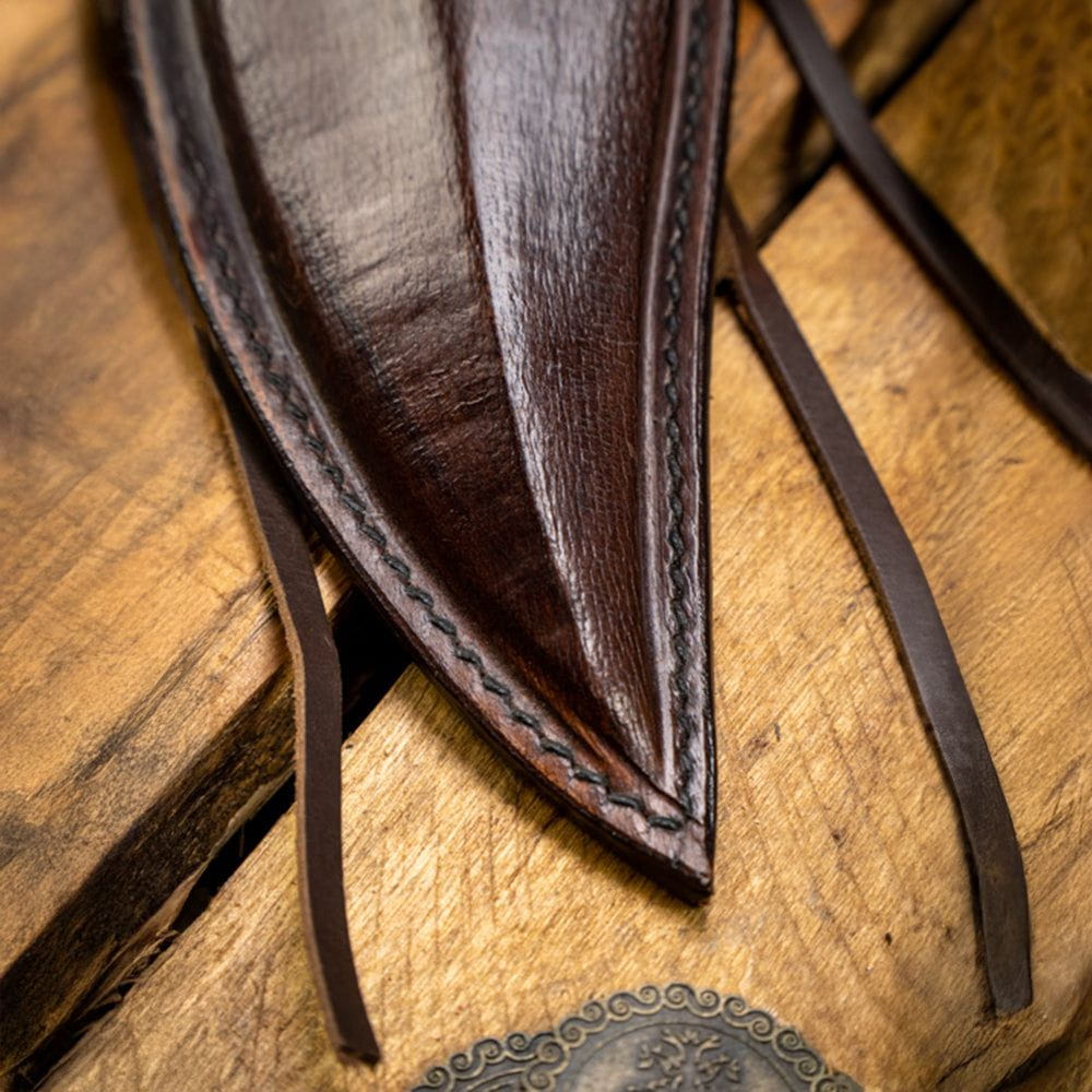 Close-up of a dark brown, hand-stitched leather Pirate scabbard with straps on a wooden surface.