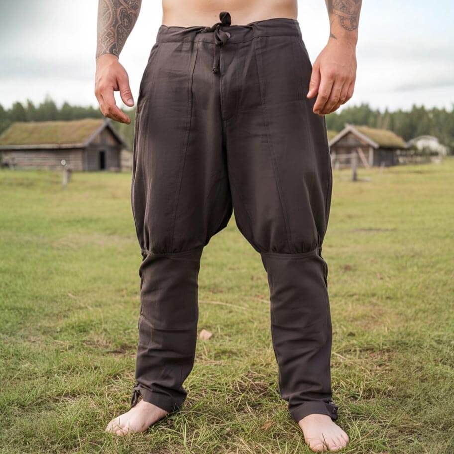 Person wearing dark brown pirate pants standing in a grassy field with wooden buildings in the background.