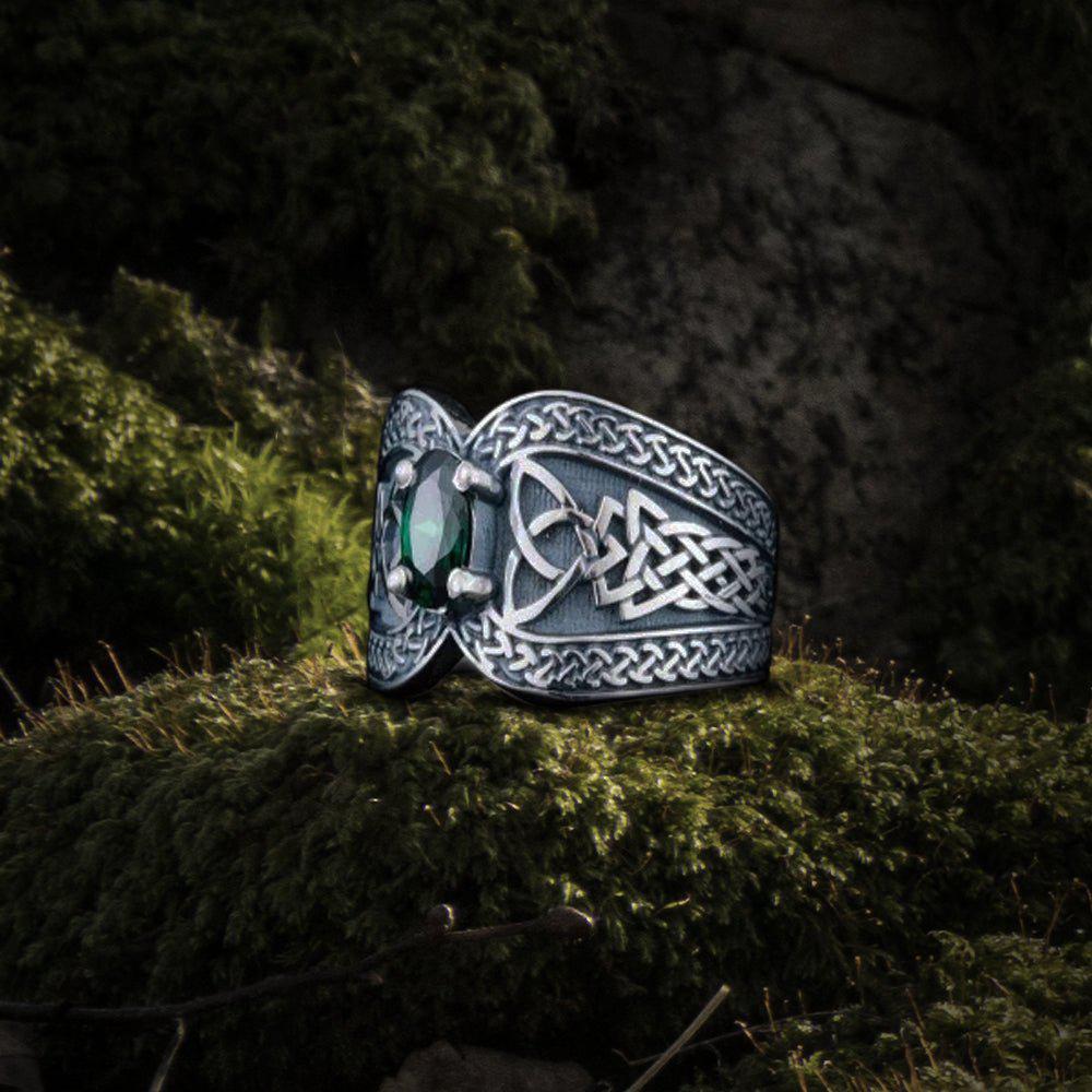 Sterling silver Pirate ring with a vibrant green cubic zirconia and Celtic knotwork on a mossy surface.
