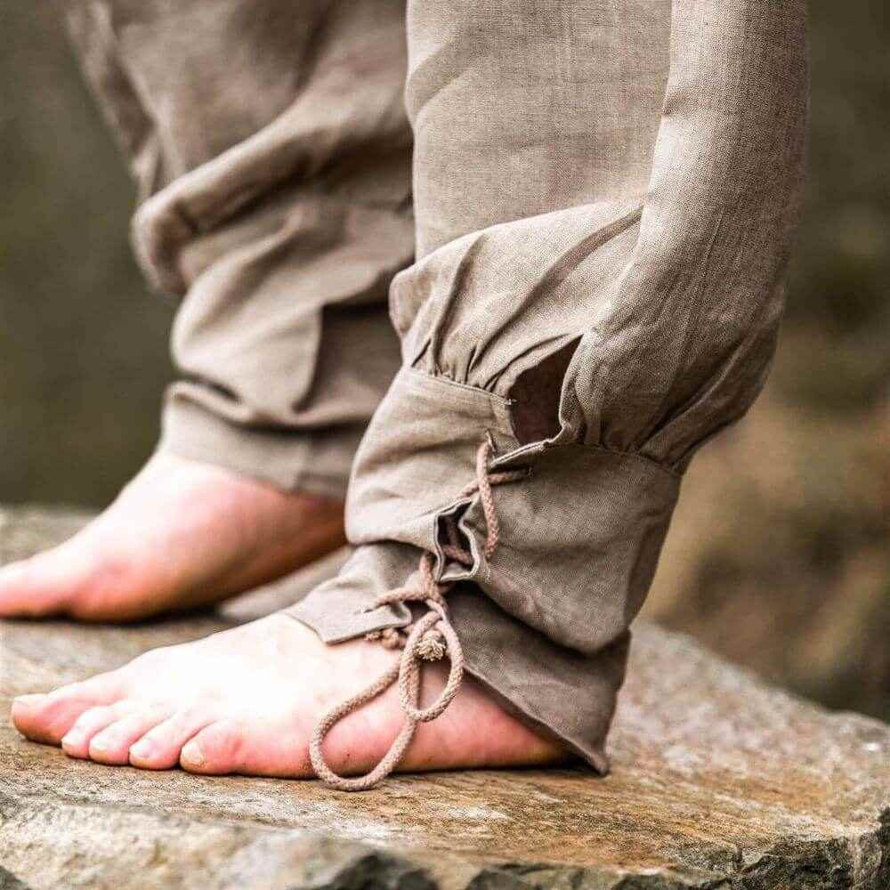 Stone grey linen Pirate pants with tapered legs and lace-up closures, worn barefoot on a rock.