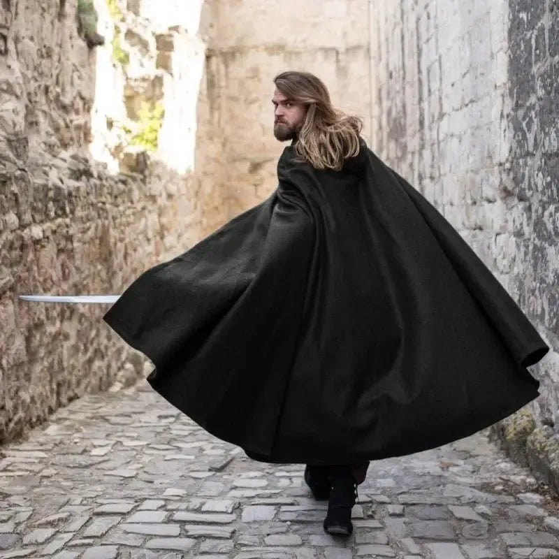 Man in a black wool Pirate cloak with a hood and wolf clasp, walking on a cobblestone path.