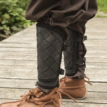 Black woven leather Pirate greaves with brass buckles worn over brown boots.