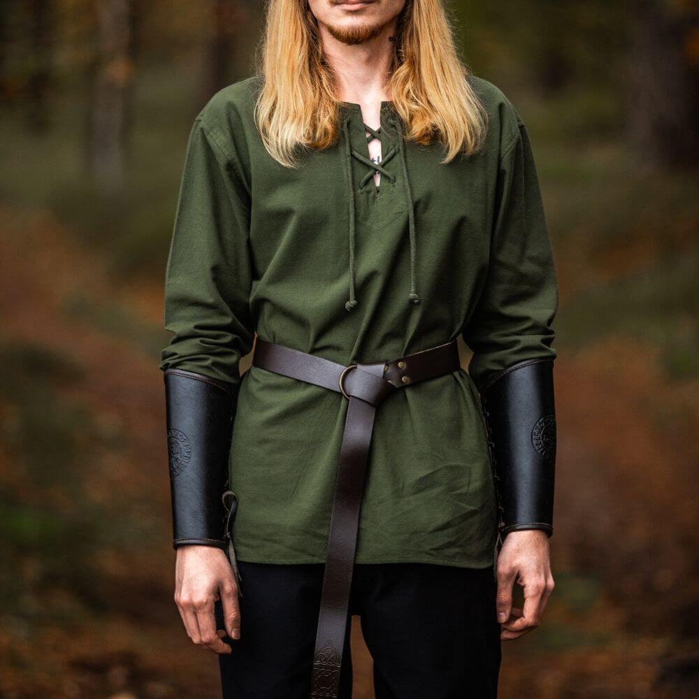 Man wearing a green Pirate tunic with long sleeves, lace-up collar, leather belt, and black arm guards in a forest