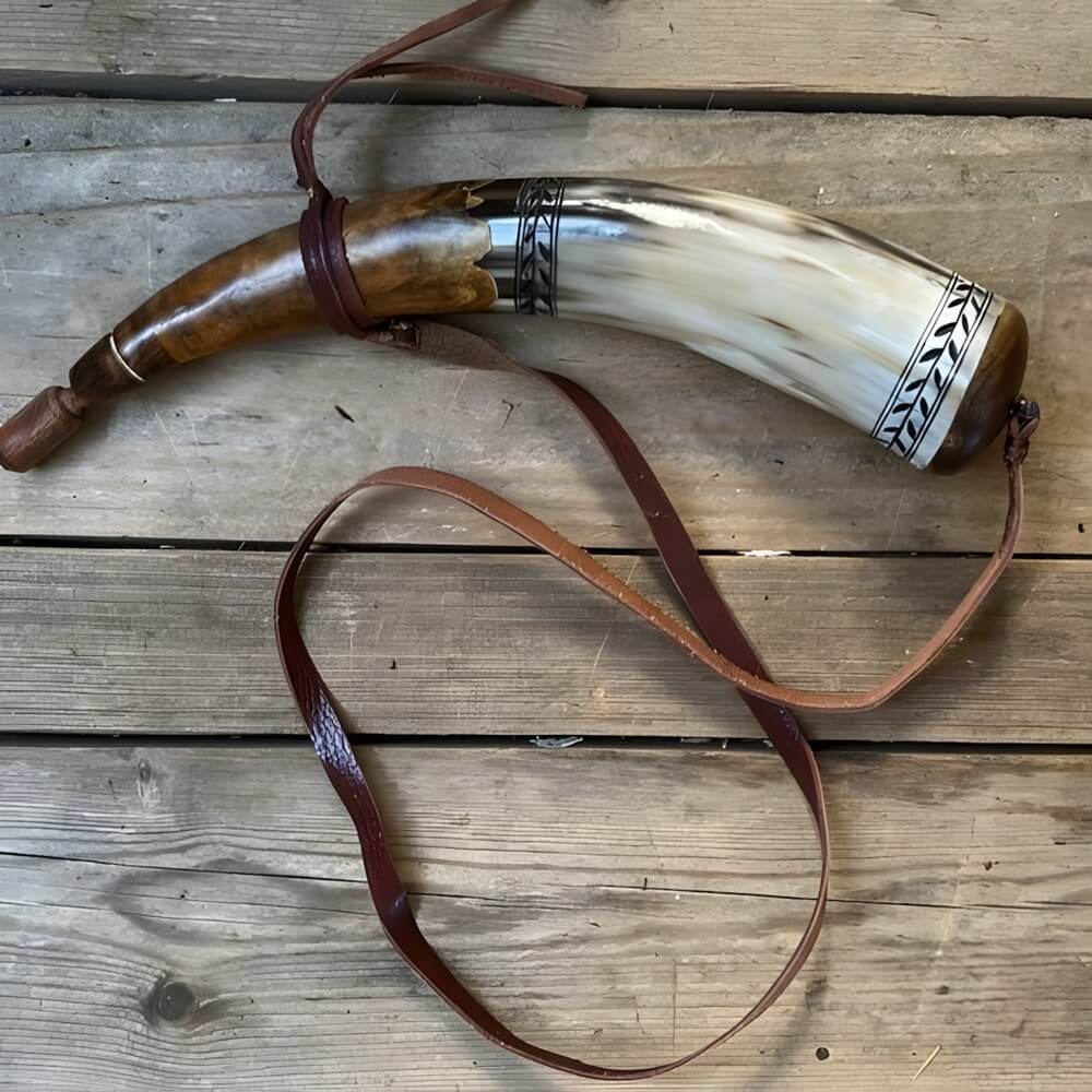 Hand-carved pirate powder horn with etched tribal bands and leather strap, resting on rustic wooden planks.