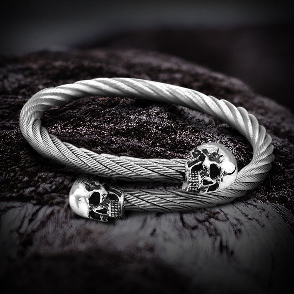 Silver stainless steel pirate bracelet with two detailed skull charms on a filigree rope-style band.