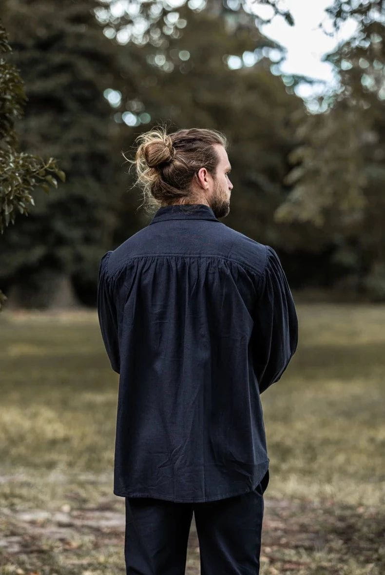 Man in a dark, loose-fitting Pirate shirt with gathered shoulders, standing in a park.