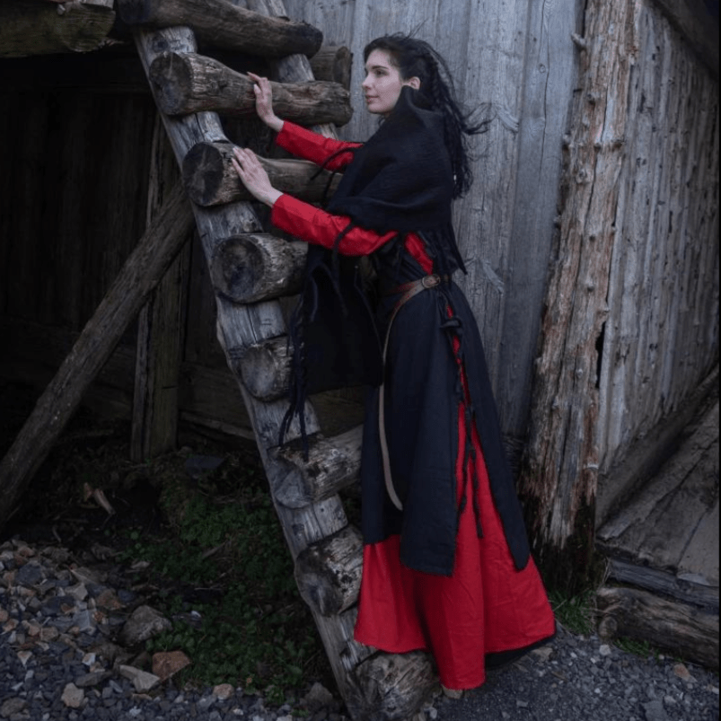Woman in a black wool Pirate stole with fringed edges, red dress, climbing a rustic wooden ladder.