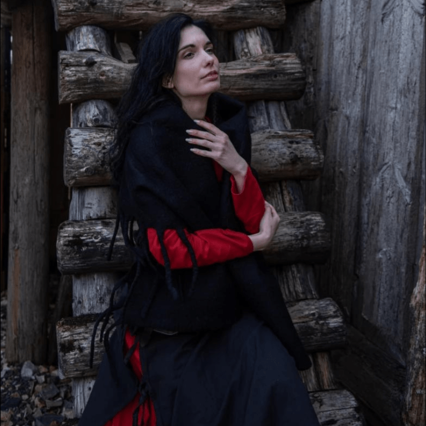 Woman wearing a black wool Pirate stole with fringed edges over a red shirt, against a wooden background.