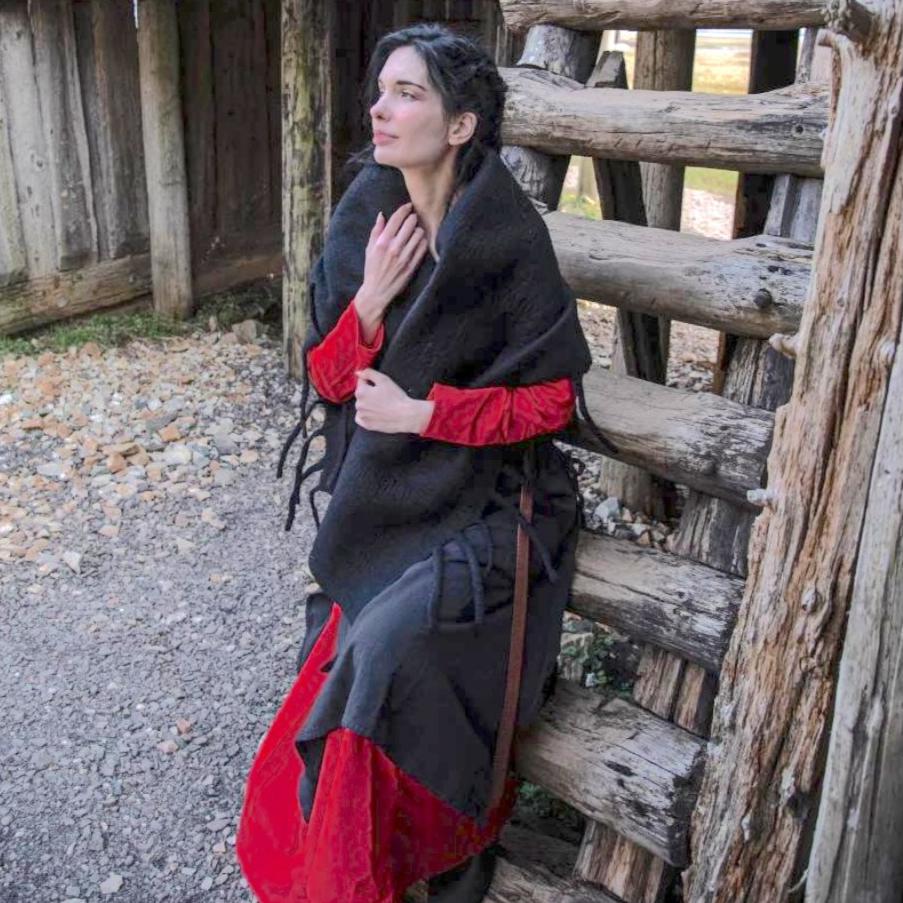 Woman in a black wool Pirate stole with fringed edges, draped over a red tunic, sitting on wooden steps.