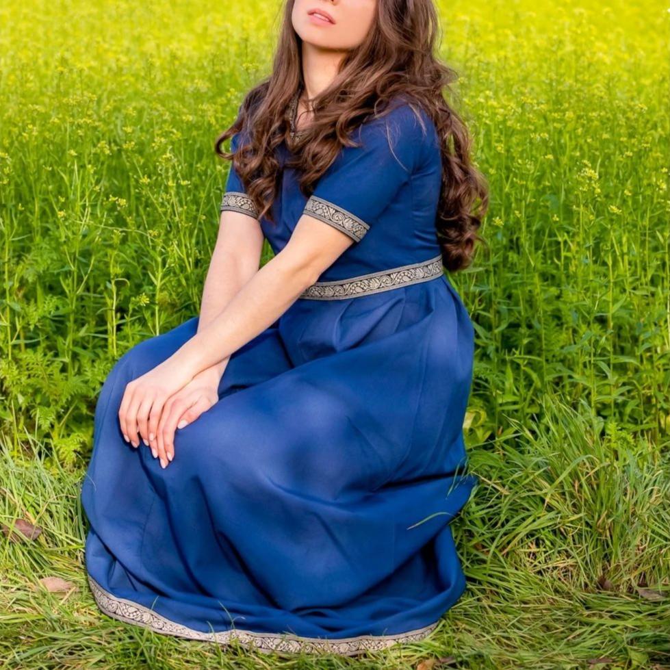 Blue Pirate Dress with intricate embroidered borders, short sleeves, and knee-length cut, worn in a field.