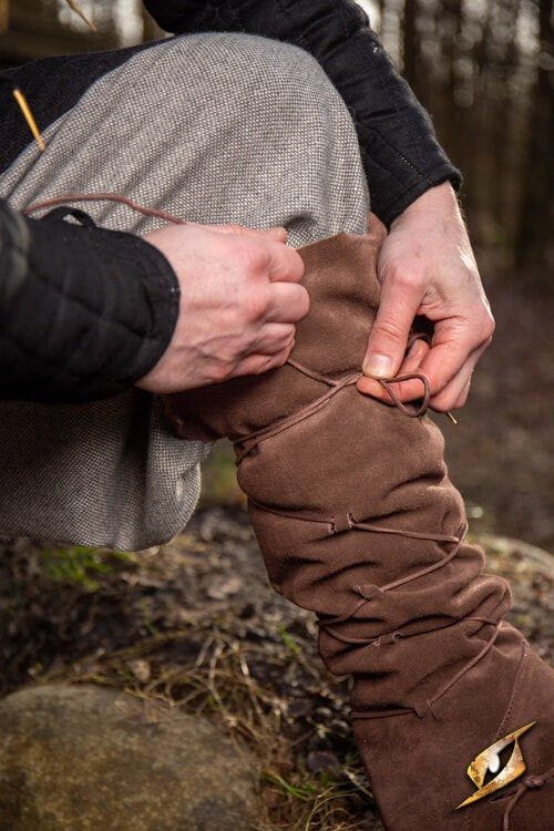 Person lacing up brown suede Pirate gaiters, transforming shoes into knee-high pirate boots.