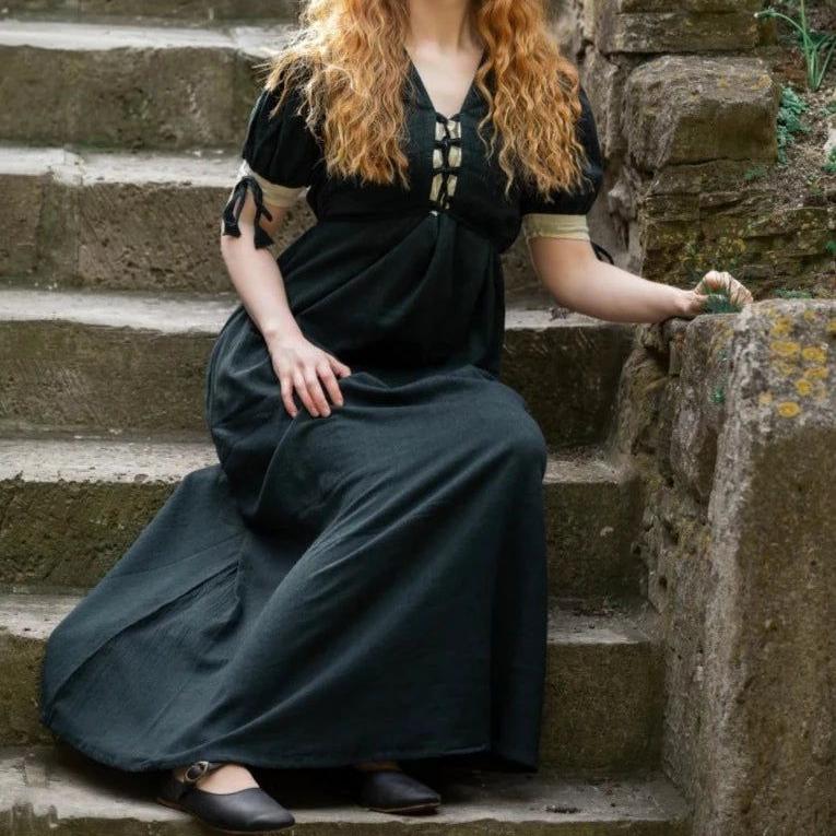 Dark green Pirate cotton gown with laced front and sleeves, worn by a woman on stone steps.