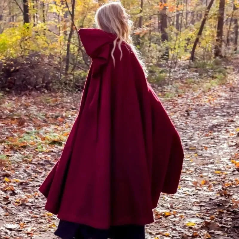 Blonde woman in a flowing, dark red hooded Pirate cloak made of heavy wool, walking on a forest path.
