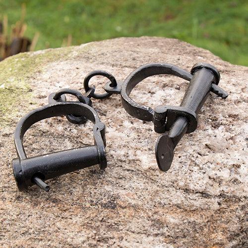 Black wrought iron Pirate manacles with hand-riveted cuffs and a working key-turned lock on a rock.