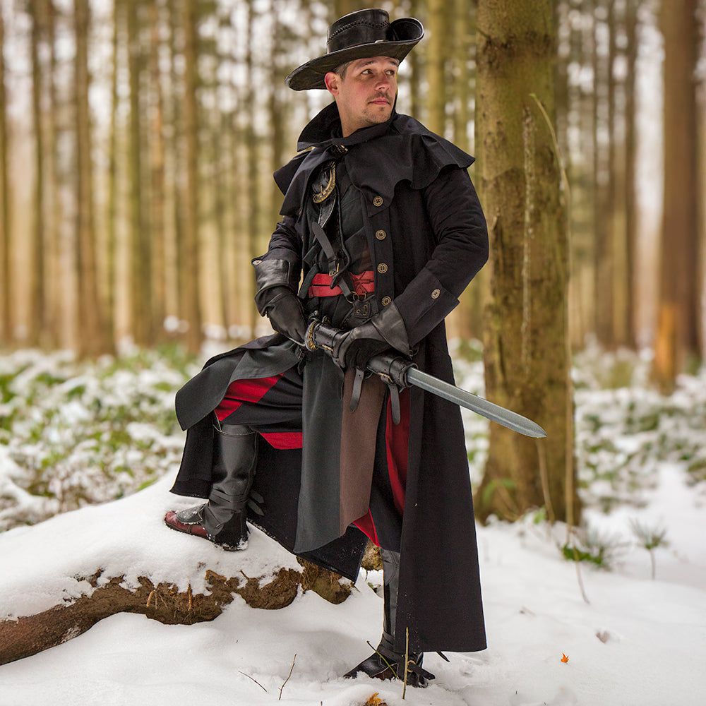Man in black canvas Pirate overcoat with removable mantle, broad collar, and ornate buttons, holding a sword in a snowy forest.