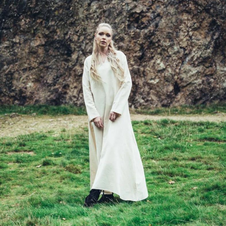 Woman in a long, natural cotton Pirate underdress with long sleeves, standing on grass.