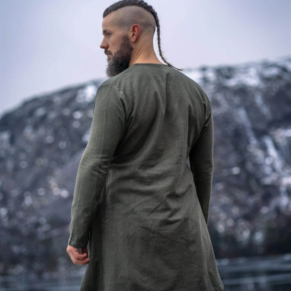 Man in olive green linen Pirate tunic with classic neckline, viewed from behind, against a snowy mountain.