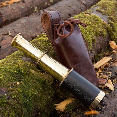 Pirate brass telescope with black leather wrap and brown leather pouch on mossy logs.