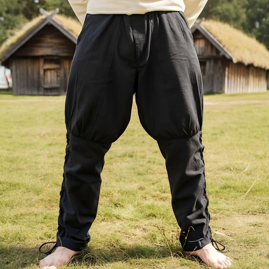 Person wearing black pirate pants standing on grass with wooden huts in the background