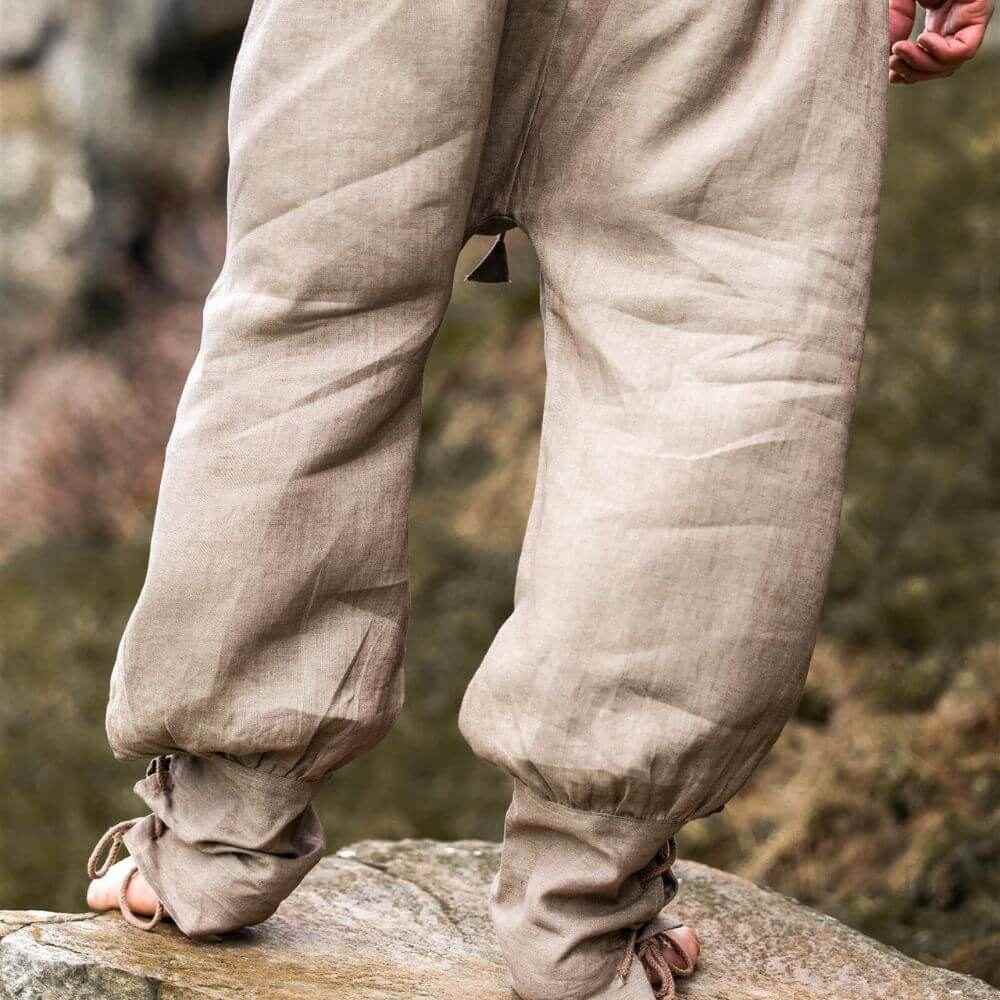 Stone grey linen Pirate pants with tapered legs and lace-up closures, worn by a person standing on rocks.