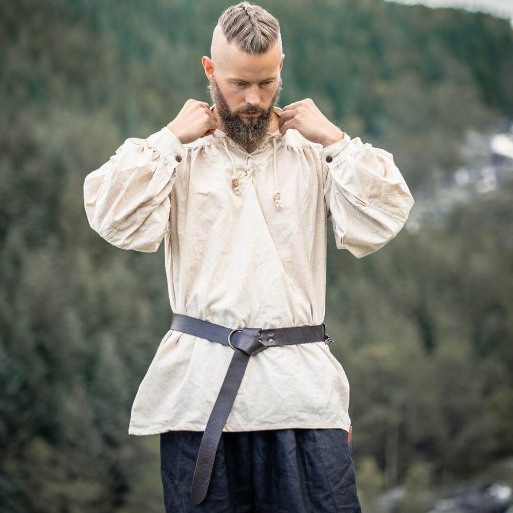 Man wearing a natural white Viking shirt with lace-up collar and puffed sleeves, belted at the waist outdoors.