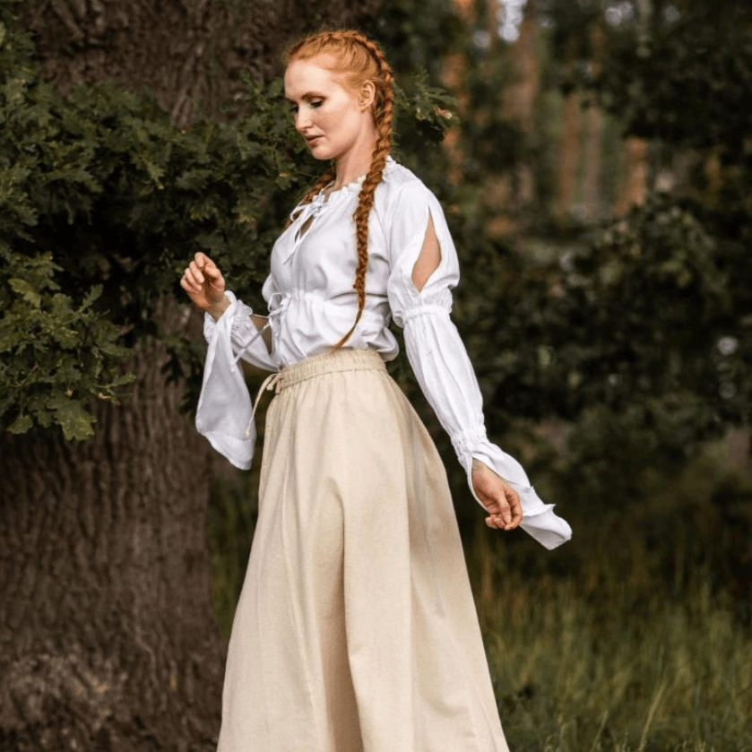 White long-sleeve Pirate blouse with ruched sleeves and adjustable waist lacing, worn with a beige skirt.