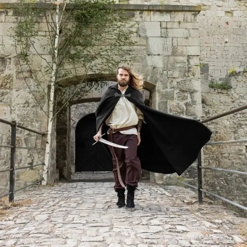 Man in black wool Pirate cloak with wolf clasp and short hood, walking with a sword.