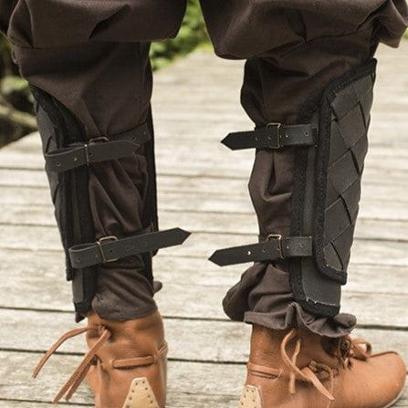 Black woven leather Pirate greaves with brass buckles over brown pants and boots.