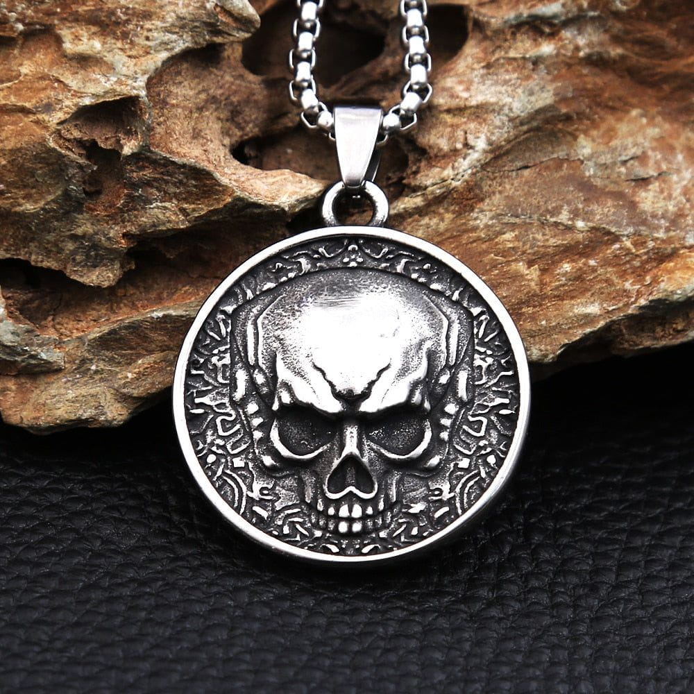 Stainless steel Pirate skull coin pendant with detailed double-sided design and chain, resting on rock.